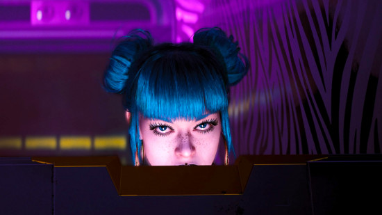 a woman with her hair in blue space buns looks over a computer at you